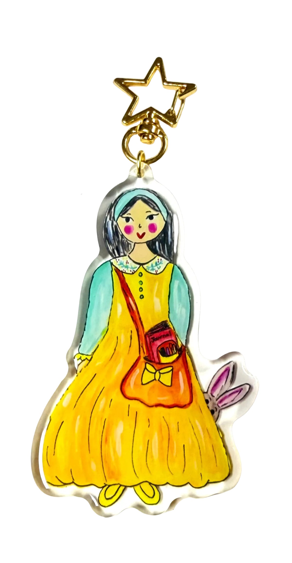 A hand-drawn acrylic keychain charm featuring a girl in a yellow dress with a teal cardigan, holding a red purse, with a gold star clasp at the top. The charm is displayed on a white background with a black text watermark reading 'ROMANTICIZE YOUR LIFE'.